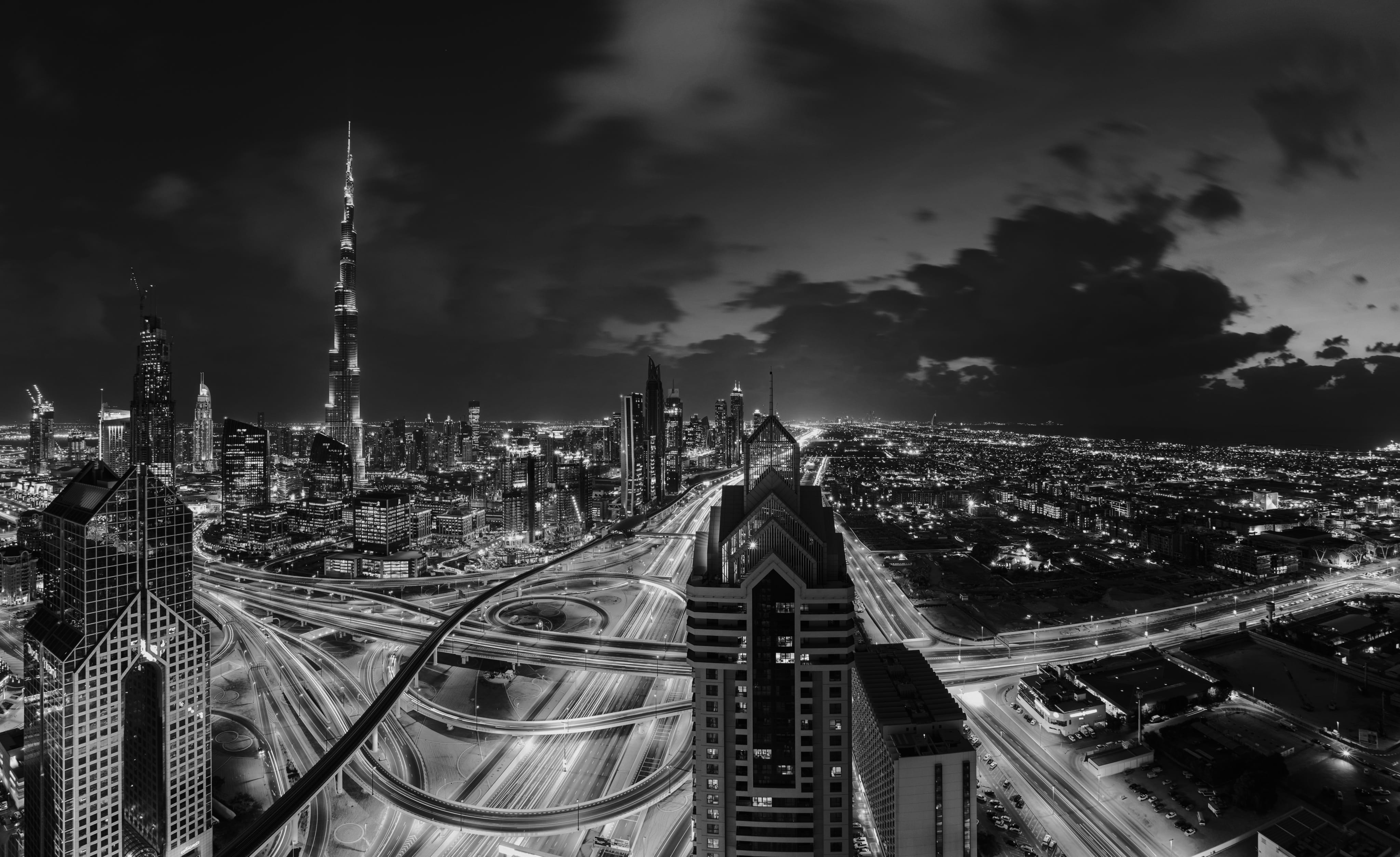 Black-and-white Dubai skyline at dusk with the Burj Khalifa and a busy highway interchange