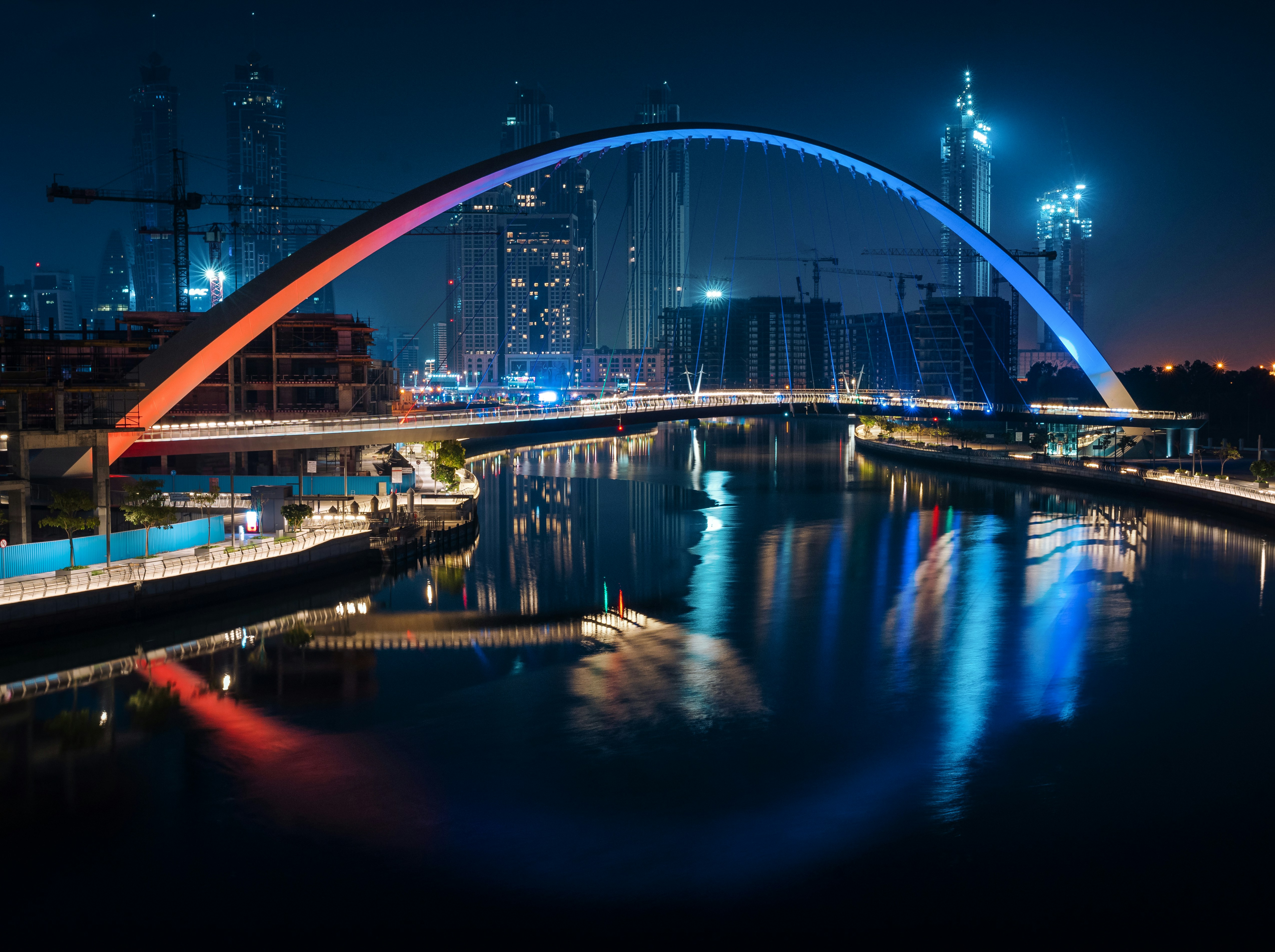 Illuminated arched footbridge over a city canal at night, lit orange and blue