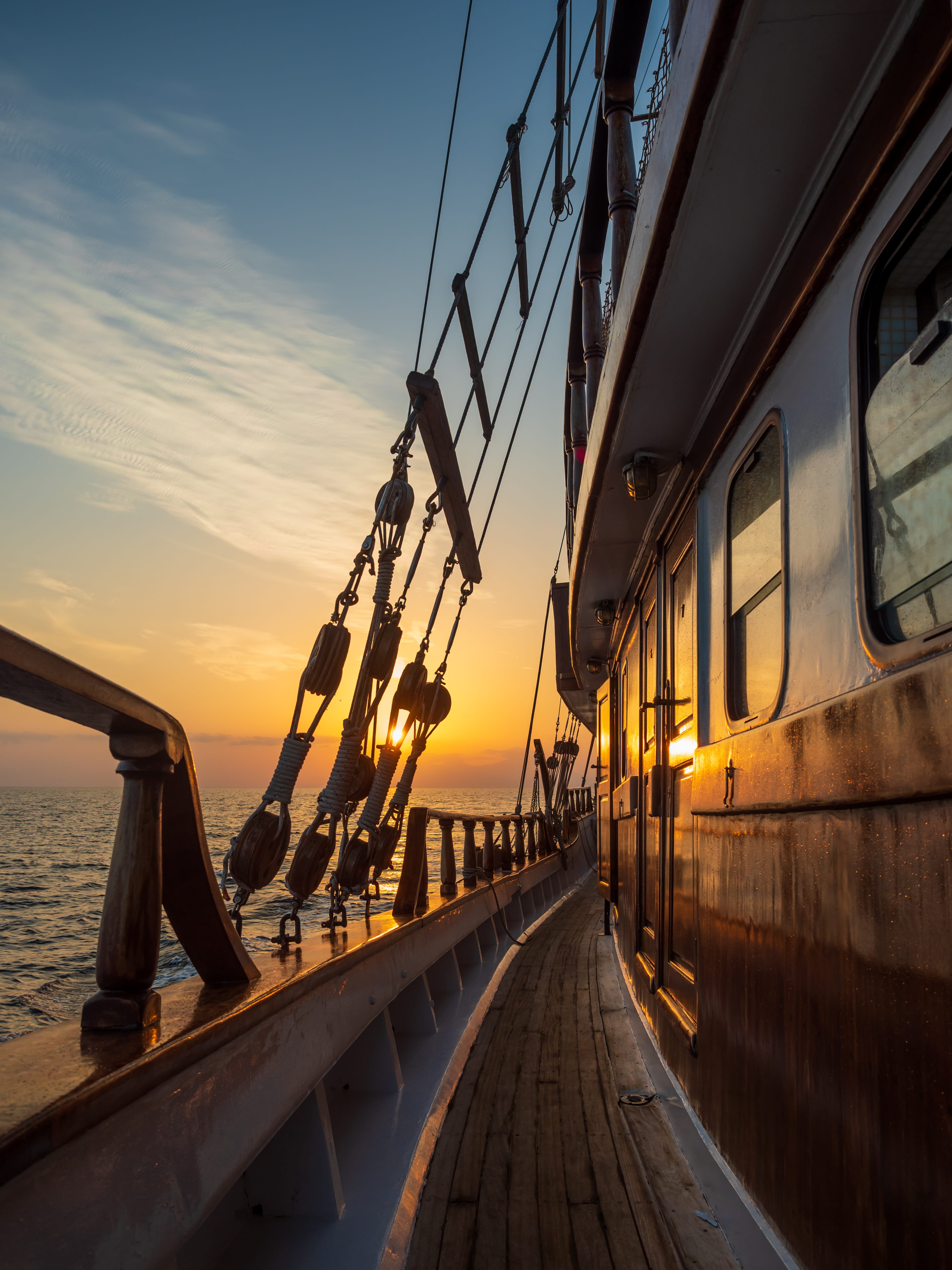Deck of a traditional sailing ship with rigging, at sunset over the sea