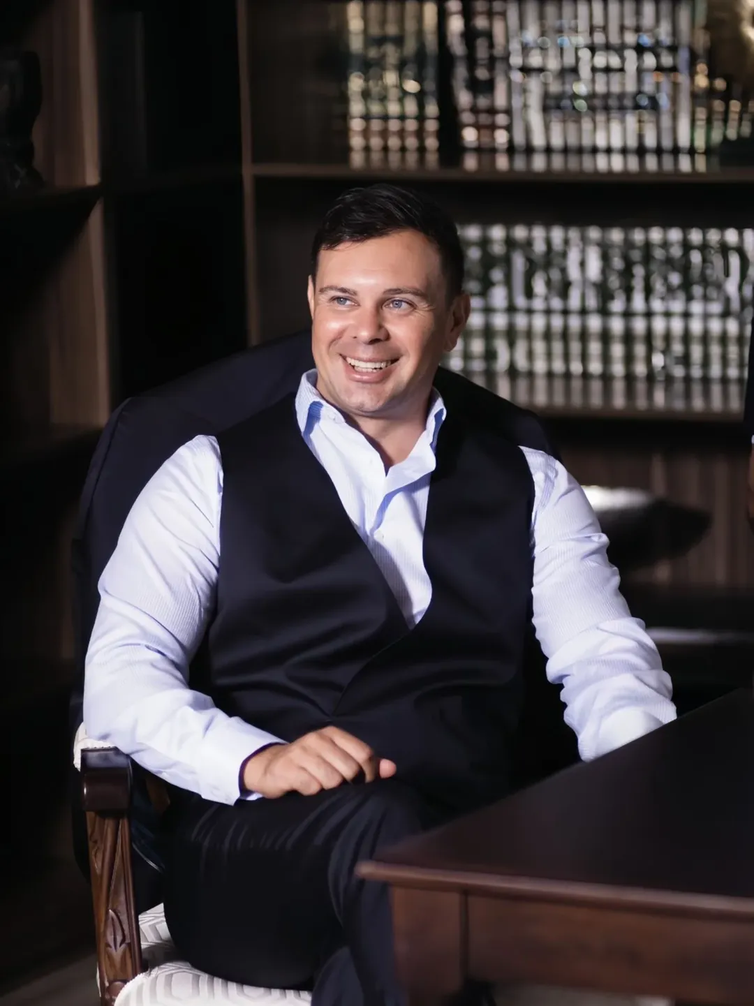 Smiling man in a waistcoat seated in a wood-panelled office