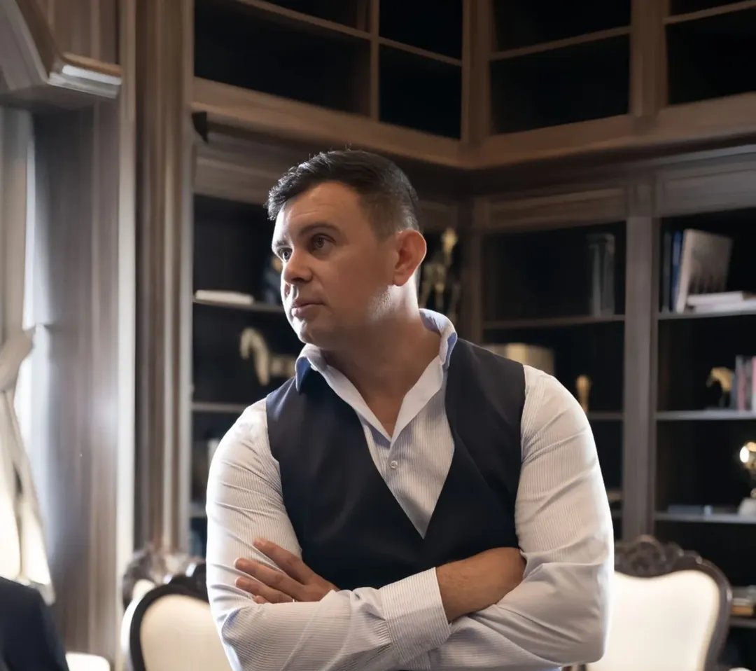 Man in a waistcoat with arms folded, listening in a wood-panelled room