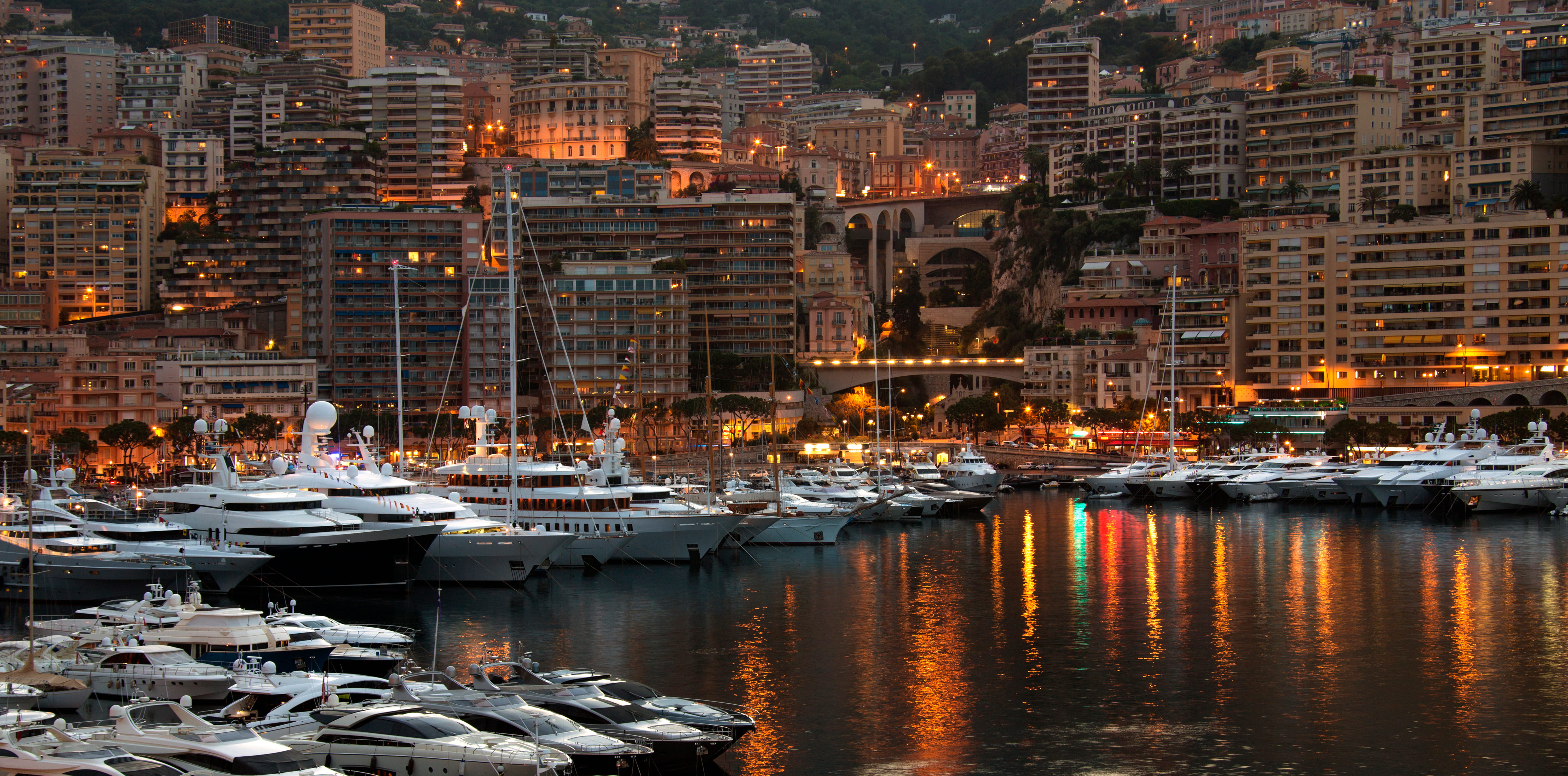 Yachts moored in Monaco harbour at dusk below hillside apartment buildings