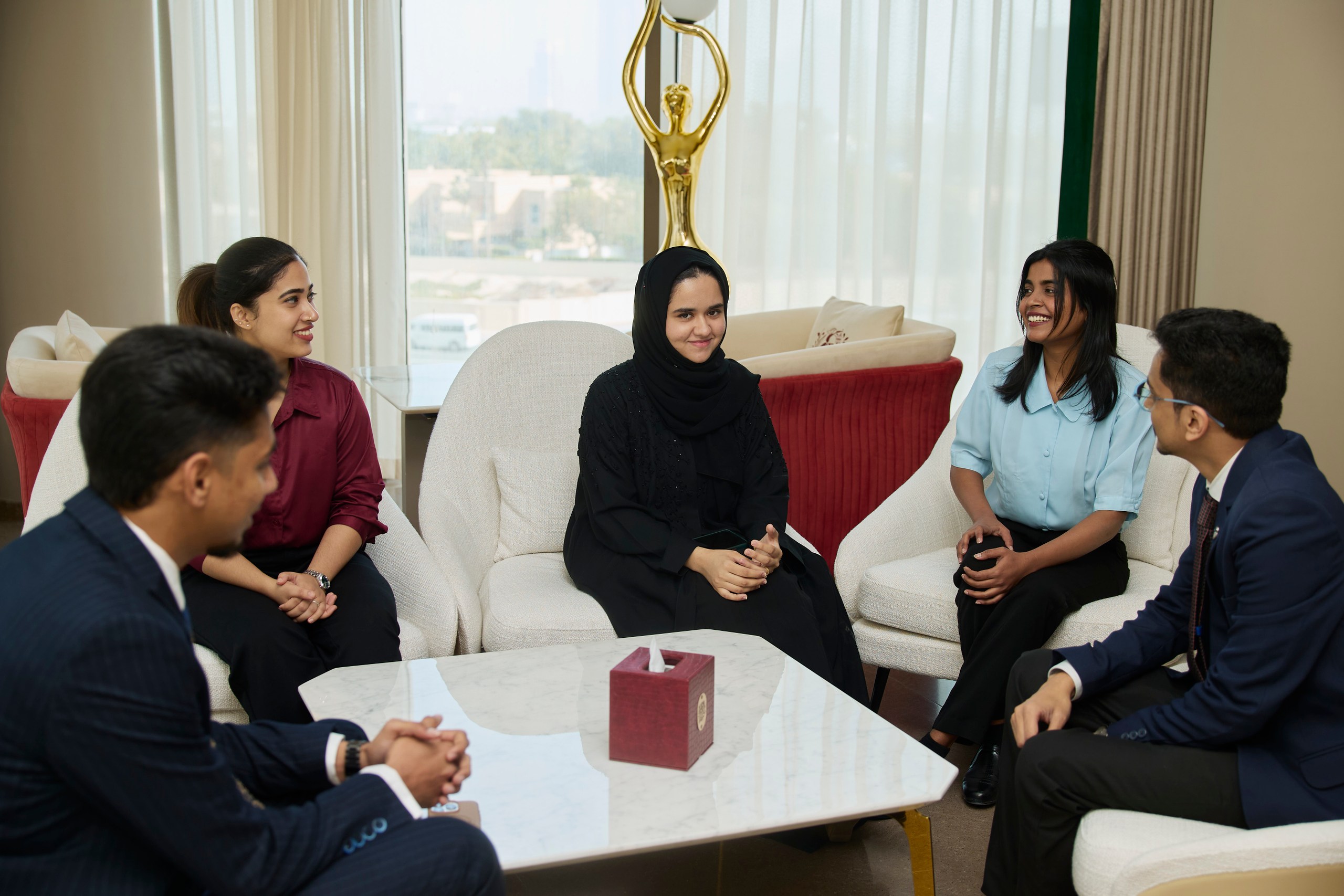 Five young professionals chatting in armchairs around a marble coffee table