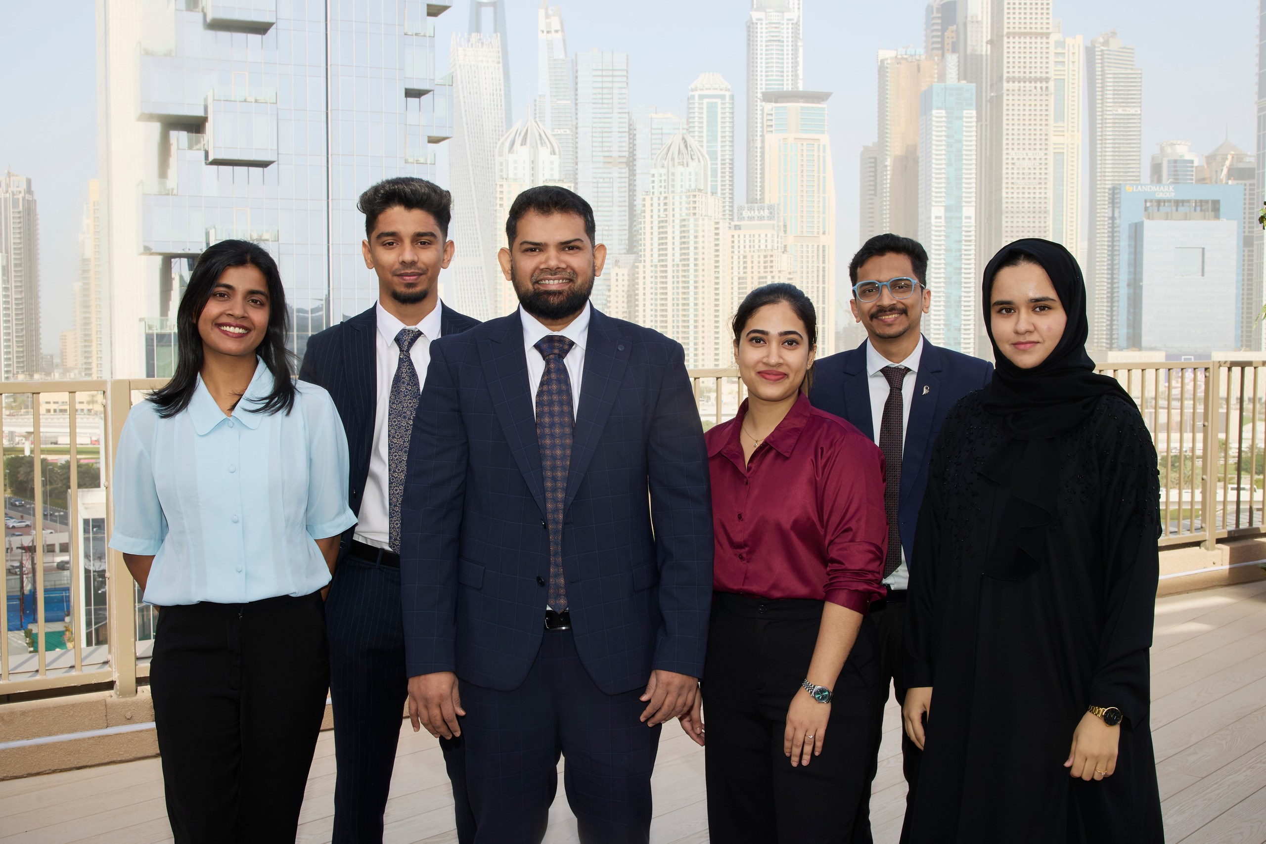 Six young professionals posing on a rooftop terrace with skyscrapers behind